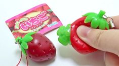 a hand is holding a strawberry shaped keychain next to a packet of candy