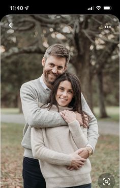 a man and woman hugging each other in front of trees