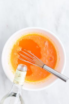 an orange liquid in a white bowl with a whisk