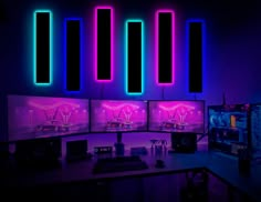 three computer monitors with neon lights on the wall above them, all in front of a keyboard and mouse