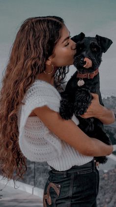 a woman holding a small black dog in her arms and kissing it's face