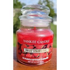 a yankee candle with strawberries on it sitting on a wooden table in front of some trees