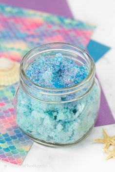 a glass jar filled with blue and purple glitter next to a starfish on top of a table