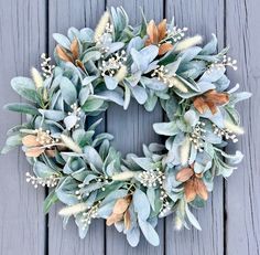 a wreath is hanging on the wall with eucalyptus leaves and white flowers in front of it