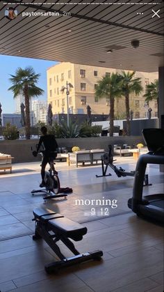 people are exercising on stationary bikes in an open gym area with palm trees and buildings in the background