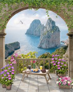 an outdoor table with flowers and fruit on it in front of a scenic ocean view