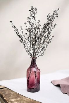 a purple vase filled with flowers on top of a wooden table next to a pink napkin