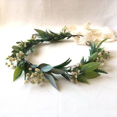 a wreath made out of leaves and flowers on a white surface with two crosses in the background