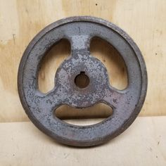 an old cast iron wheel with holes in the center on a wooden surface next to a wall