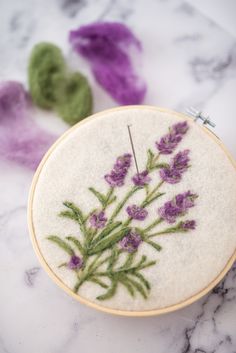 a close up of a embroidery on a table with some scissors and purple flowers in the background