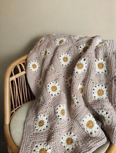 a crocheted blanket with daisies on it sitting on a wicker chair