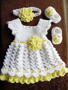 a crocheted baby dress and booties on a brown blanket next to a pair of slippers