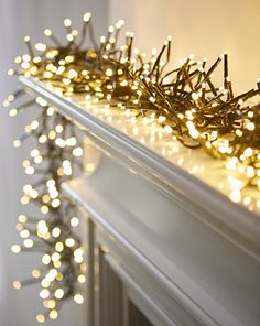 a white mantle covered in christmas lights next to a fire place with a wreath on top