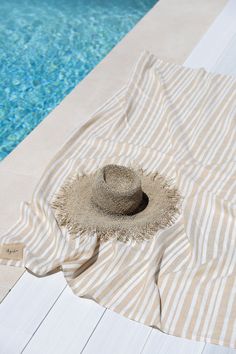 a hat sitting on top of a beach towel next to a swimming pool with blue water