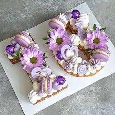 two cakes decorated with purple flowers on top of a white table cloth, one has the letter e and the other is made out of doughnuts