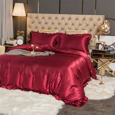 a bed with a red comforter and pillows on top of white fluffy rugs