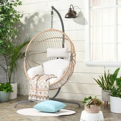 a hanging chair with pillows on it next to potted plants