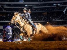 a woman riding on the back of a brown horse in an arena with people watching