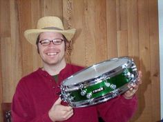 a man in a cowboy hat is holding a green and silver snarel drum