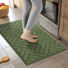 a woman in grey leggings standing on a green rug next to an oven