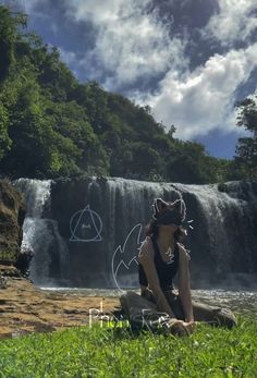 a woman sitting on top of a rock next to a waterfall