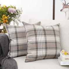 two plaid pillows sitting on top of a white couch next to a vase with flowers