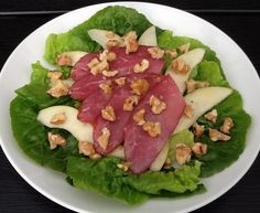 a white plate topped with lettuce covered in meat and nuts on top of it