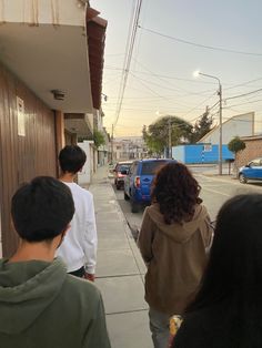 a group of people walking down a sidewalk next to a blue car and building with cars parked on the side walk