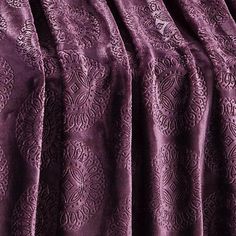 the purple bedspread is made up with an intricate pattern and pleated edges