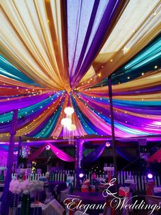 the inside of a wedding tent decorated with multicolored draping and chandeliers