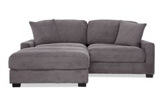 a gray sectional couch with pillows on the arm and foot rest in front of it