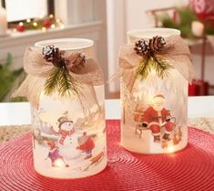 two glass jars with christmas decorations and lights in them sitting on a red place mat