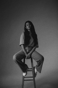 a black and white photo of a woman sitting on top of a wooden stool with her legs crossed