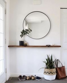 there is a mirror on the wall above a shelf with shoes and a plant in it