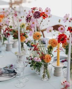 the table is set with many different flowers in vases and candles on each side