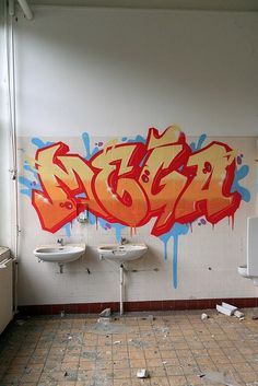 a bathroom with graffiti on the wall next to two urinals and sinks in it