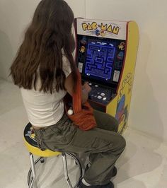 a woman sitting in front of an old fashioned arcade game machine playing pac - man