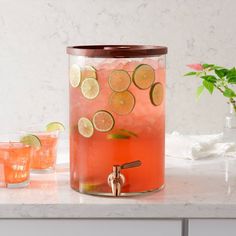 a pitcher with lemons and limes on it sitting on a counter next to two glasses