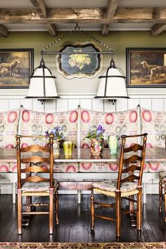 a dining room table with four chairs and two lamps on the wall above it, in front of an ornately decorated couch