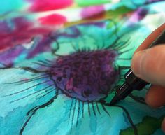 a person is writing on a colorful fabric with a black ink pen in their left hand