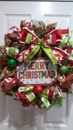 a christmas wreath hanging on the front door with merry christmas written in red, green and white