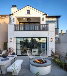 an outdoor fire pit in front of a white house with patio furniture and potted plants