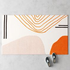 two pairs of shoes are on the floor next to an orange and white area rug