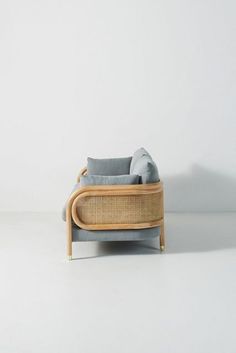 a couch made out of wicker and grey fabric on a white floor with a mirror in front of it