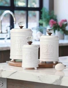 three white canisters sitting on top of a kitchen counter next to a window