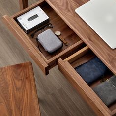 an open drawer on a wooden table with various items in it and a laptop computer