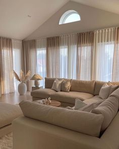 a living room filled with lots of furniture next to tall window covered in sheer curtains