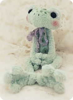 a green stuffed animal sitting on top of a white bed covered in lacy fabric and lace