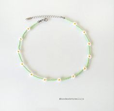 a green beaded bracelet with white and yellow flowers on it's end is shown