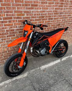 an orange dirt bike parked next to a brick wall